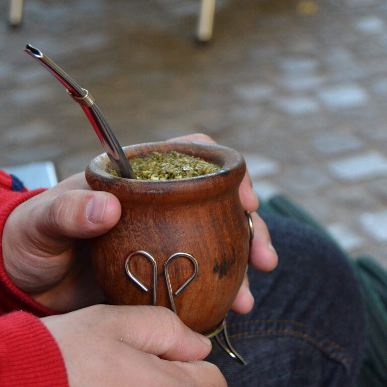 manos sostenienod mate de madera con yerba mate