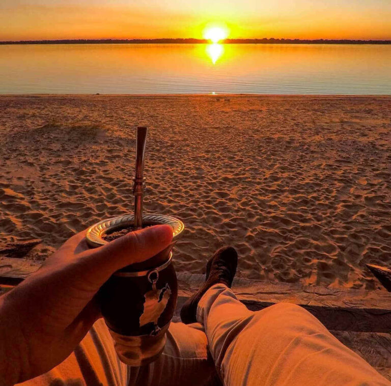 hombre tomando mate e la playa en un atardecer